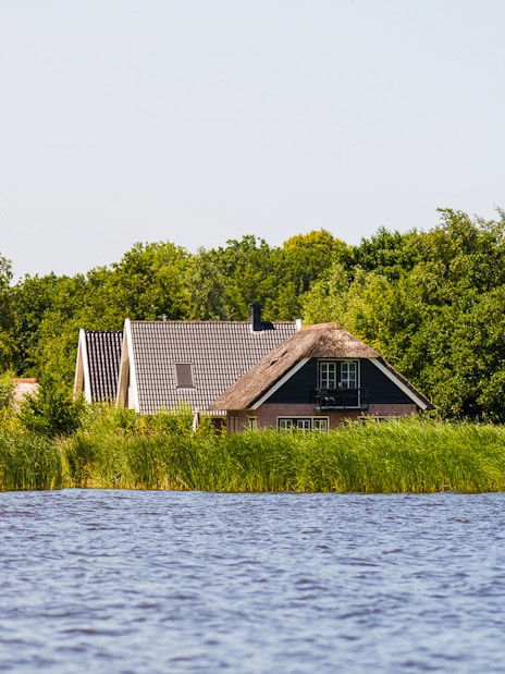 Traditional houses by the water in Giethoorn, surrounded by greenery, seen on a day trip from Amsterdam.