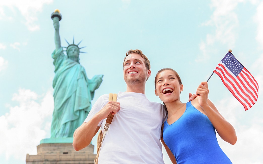 Couple smiling near Statue of Liberty holding American flag, New York City.