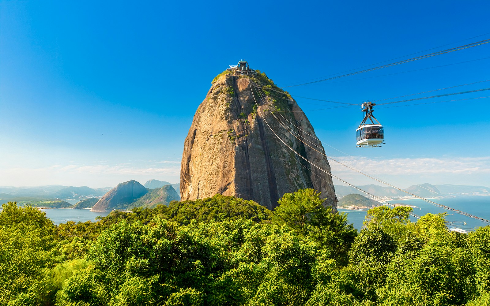 Cable car ascending Sugarloaf Mountain, Rio de Janeiro, with cityscape and ocean view.
