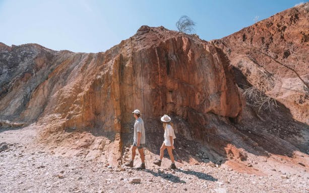 Two people walking near rocky cliffs in Uluru-Kata Tjuta, Australia.
