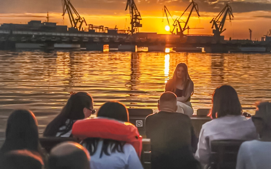 Guests enjoying a sunset view of Gdansk Shipyard during a river cruise on a historical boat.
