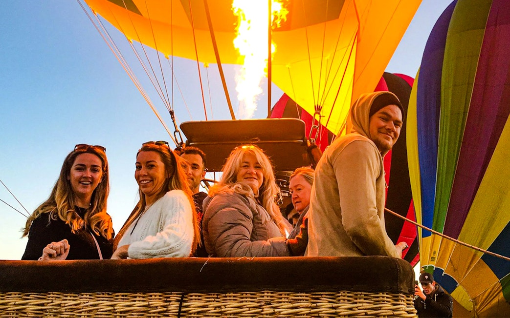 Group enjoying a hot air balloon ride with colorful balloons in the background.