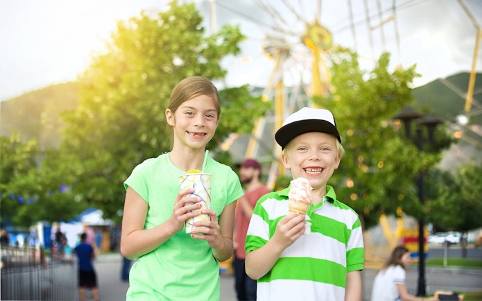 Kids enjoying ice cream at an amusement park with a Ferris wheel in the background.