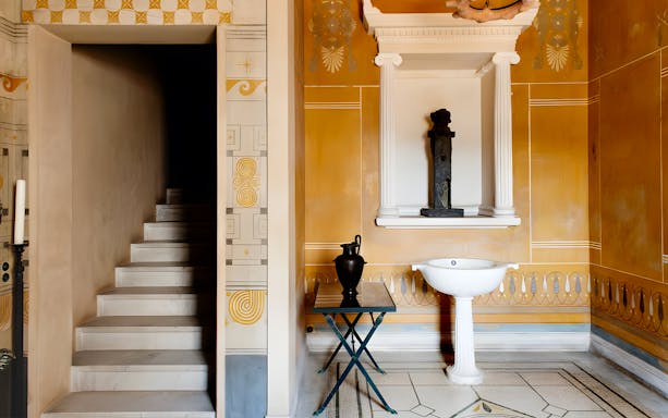 Interior of Villa Kerylos with ornate wall designs, a staircase, and classical decor.