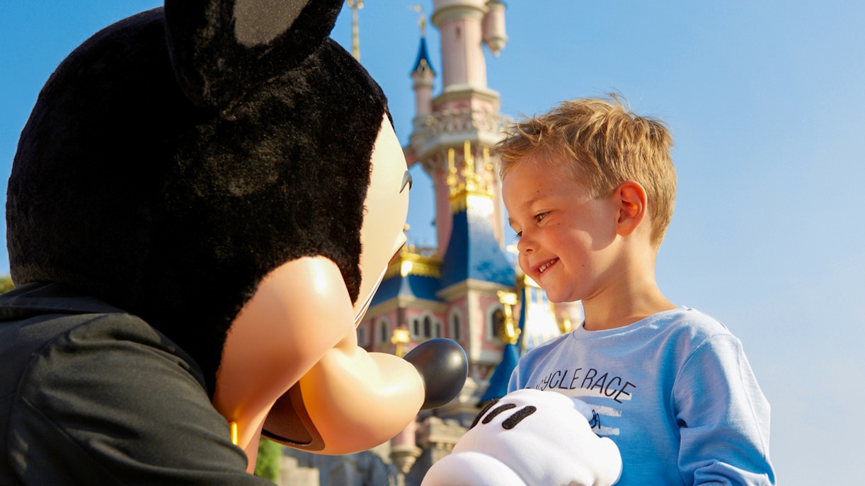 Child meeting Mickey Mouse at Disneyland Paris with castle in background.