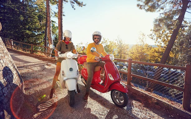 Participants on Vespa tour in Fermo, Italy, riding through scenic village path.
