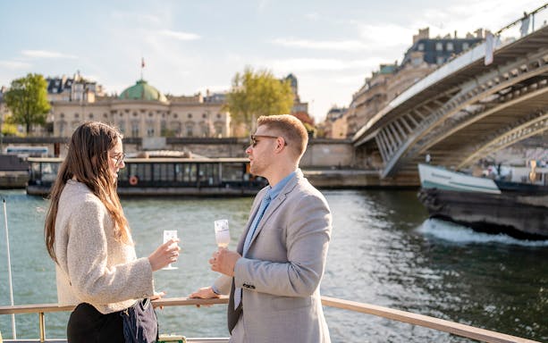 People enjoying champagne on a Seine River cruise in Paris with a bridge in the background.
