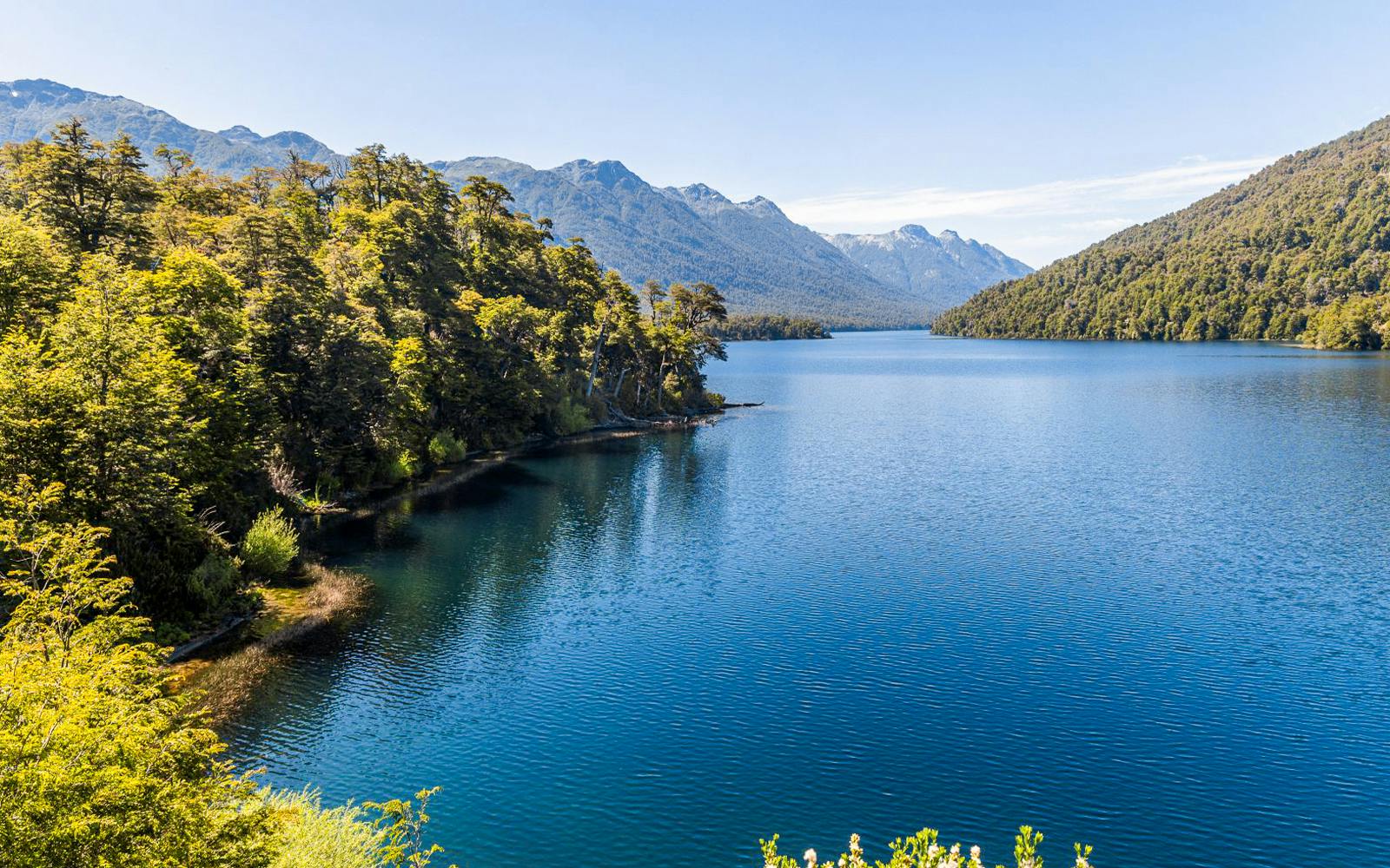 Patagonian lake with clear water, surrounded by forests and mountain peaks.