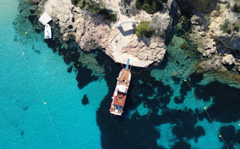 Boat docked at rocky coastline with clear turquoise water, Beach Hopper Cruise Ibiza.