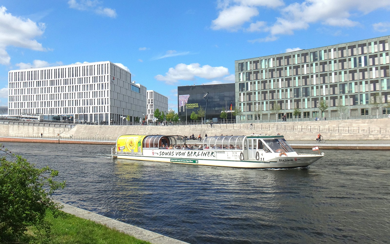Berlin sightseeing cruise boat on the Spree River near modern buildings.