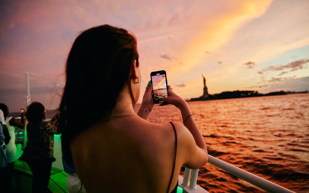 Woman taking photo of Statue of Liberty during New York evening cruise.