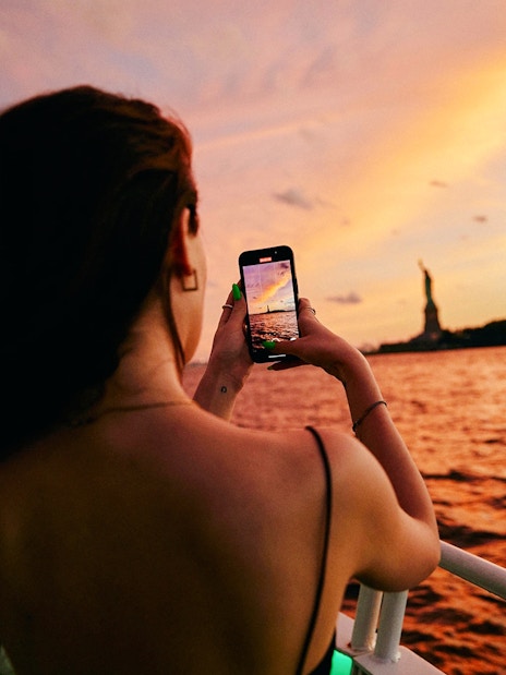 Woman taking photo of Statue of Liberty during New York evening cruise.