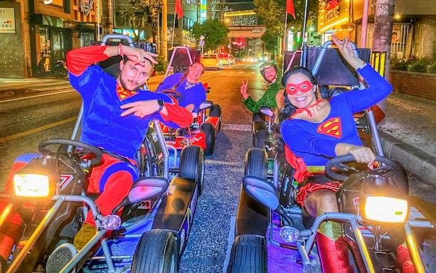 Group in superhero costumes enjoying go-karting on a street in Okinawa at night.