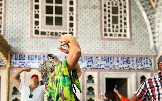 Visitors photographing ornate tiles inside Topkapi Palace during a guided tour in Spanish.
