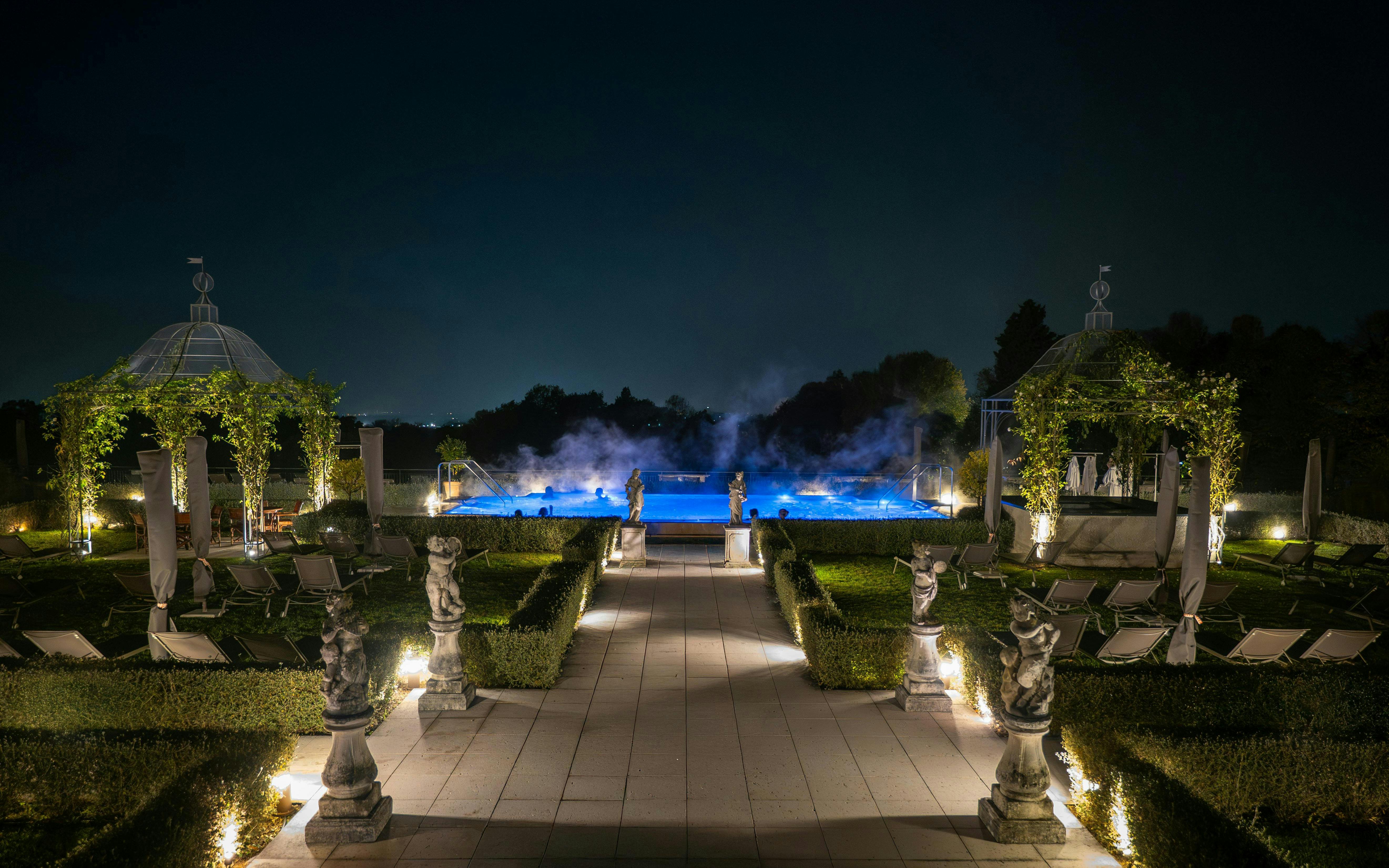 Exteriors of QC Terme Garda at night with illuminated pool and garden statues.