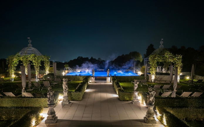 Exteriors of QC Terme Garda at night with illuminated pool and garden statues.