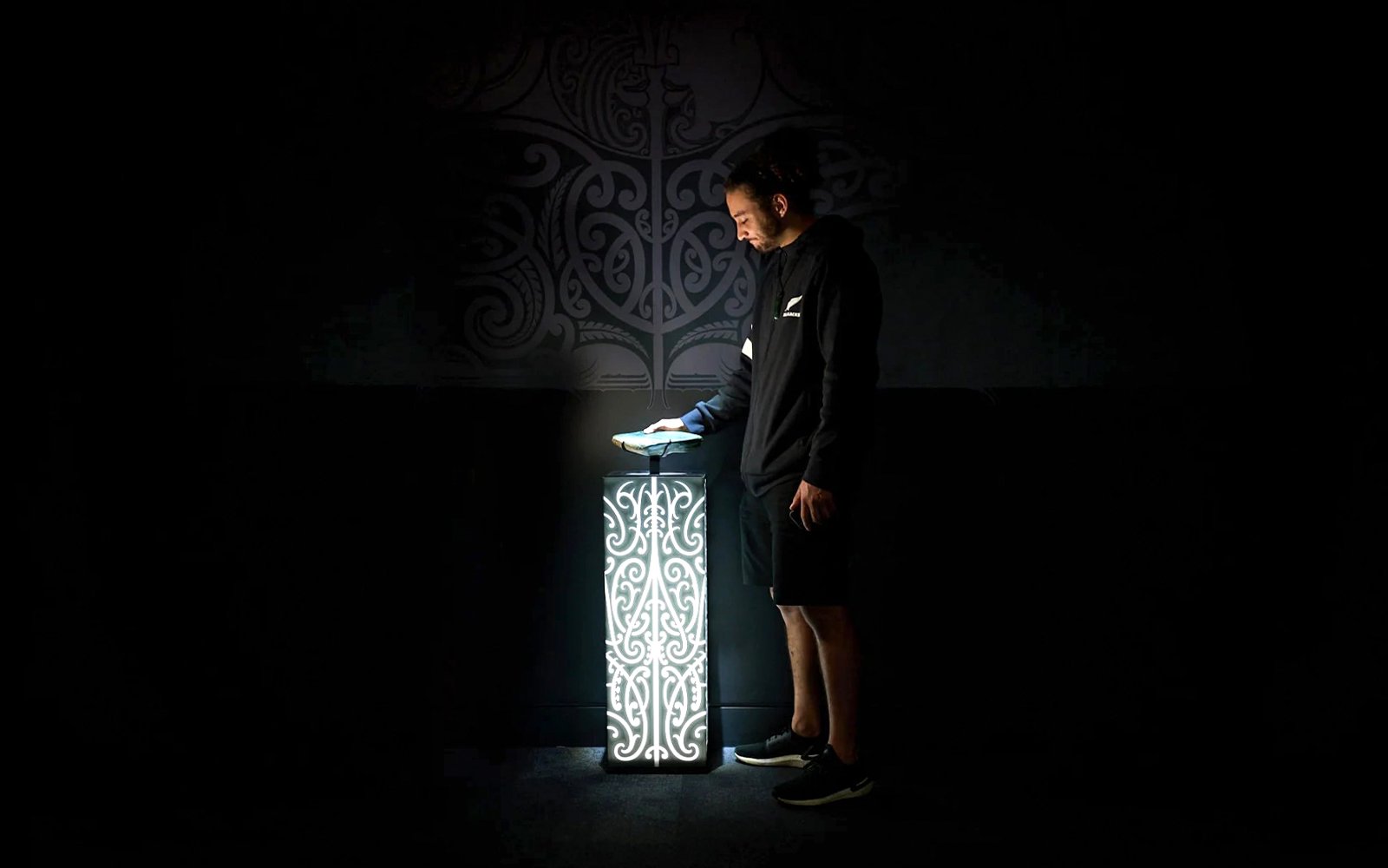 Person interacting with illuminated Maori design at All Blacks Experience, New Zealand.