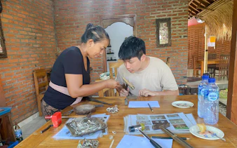 Jewelry making class in Ubud, Bali, with instructor guiding a participant using tools.
