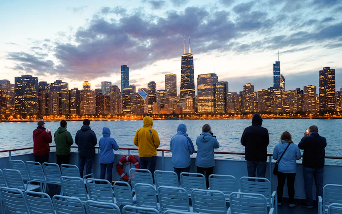 People on a boat deck viewing Chicago skyline at dusk with water and cloudy sky.
