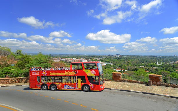 City sightseeing bus on a hill overlooking Johannesburg skyline.