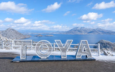 TOYA sign with snowy Lake Toya and mountains in Hokkaido background.