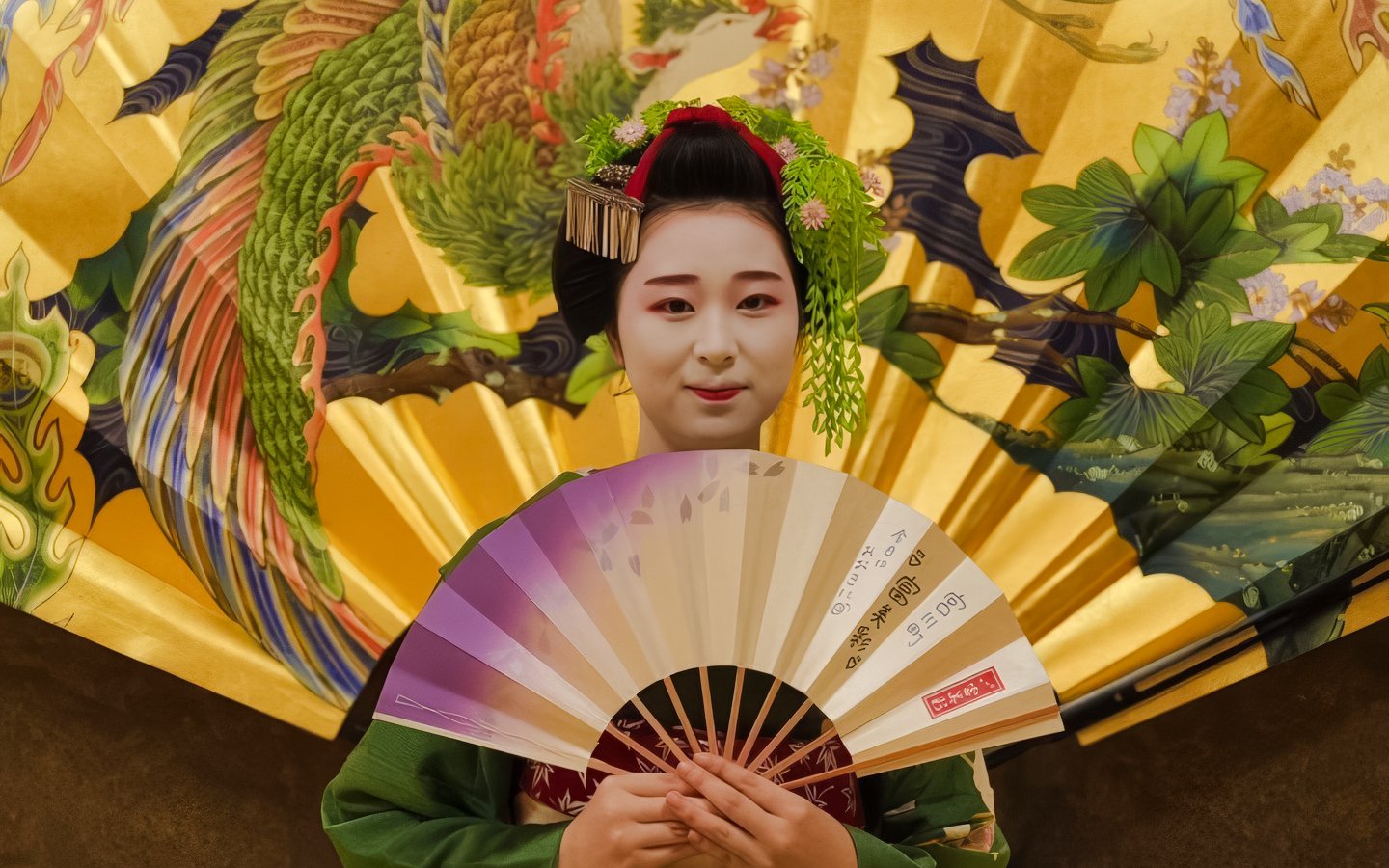 Geisha holding a fan in front of a decorative Japanese screen.