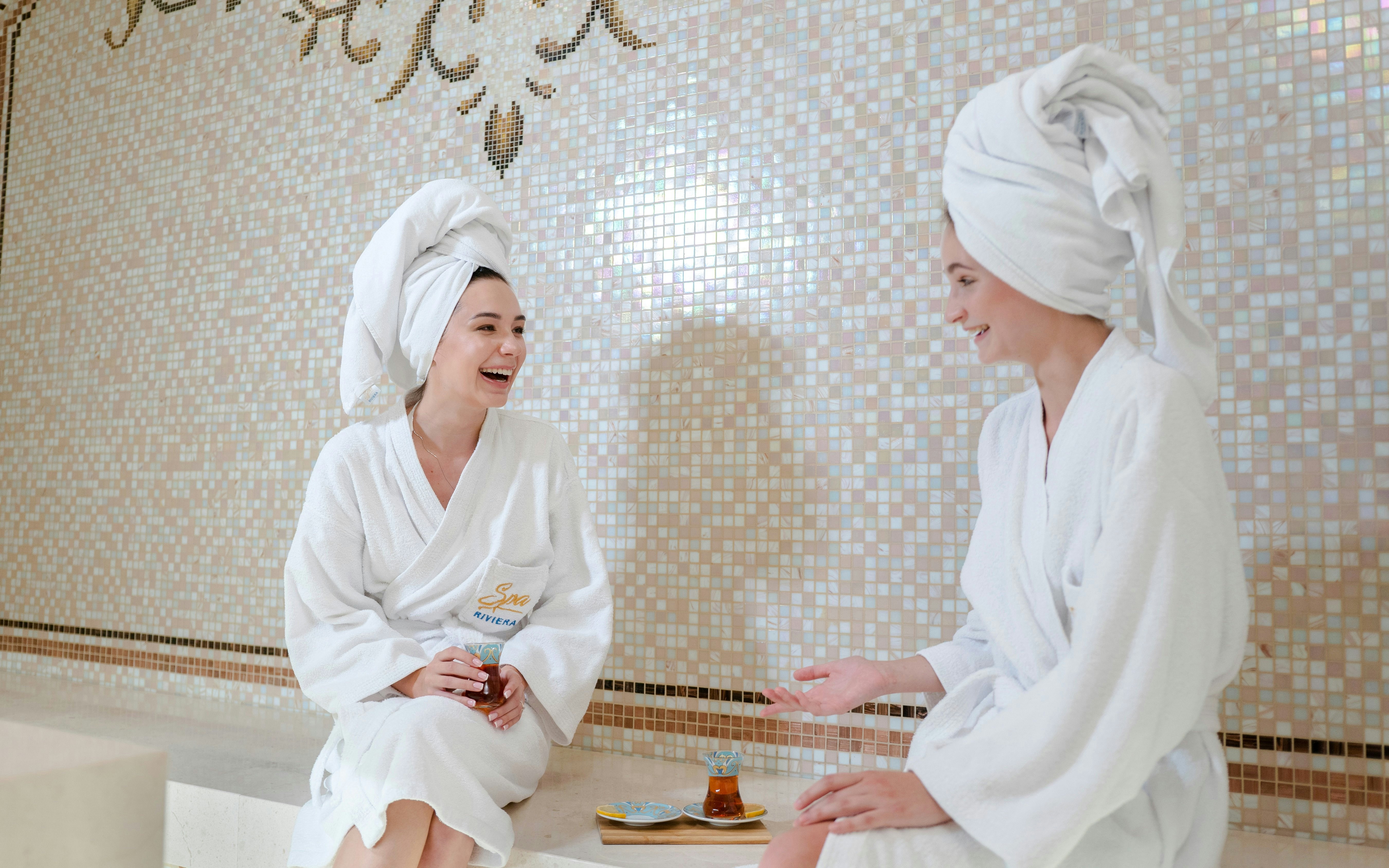 Girls relaxing and chatting in a hamam, wearing robes and towels.
