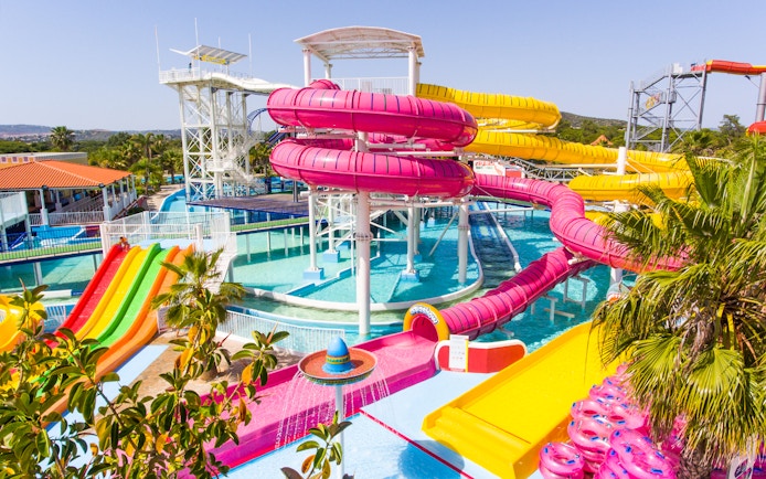 Colorful water slides at Aquashow Water Park, Portugal, with palm trees and clear blue pools.