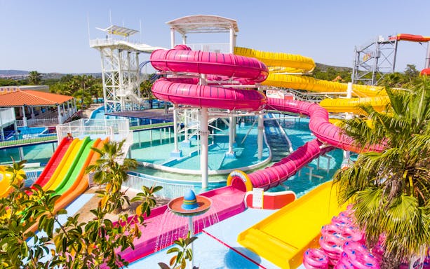 Colorful water slides at Aquashow Water Park, Portugal, with palm trees and clear blue pools.