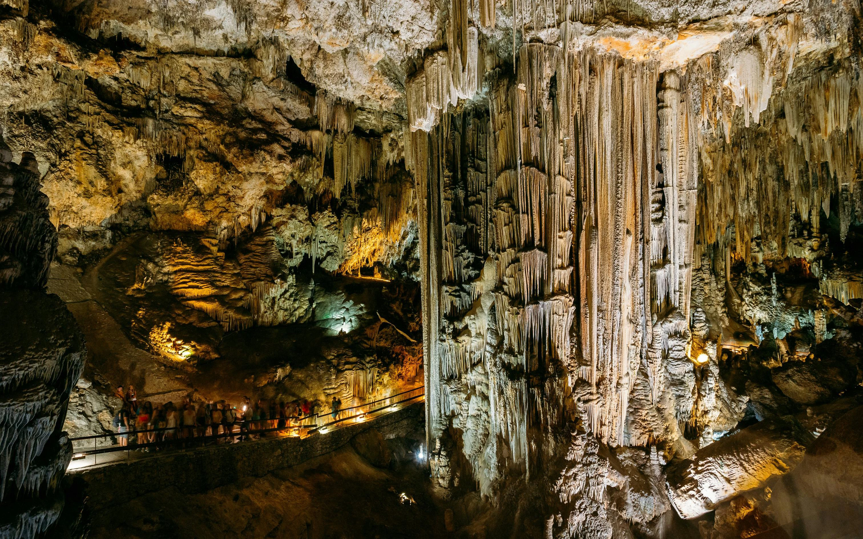 Stalactites and stalagmites in the illuminated Caves of Nerja, Spain, with visitors on a walkway.