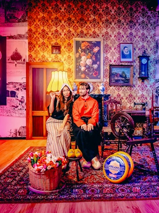 Guests in traditional Dutch attire with tulips and cheese in Holland-themed room.
