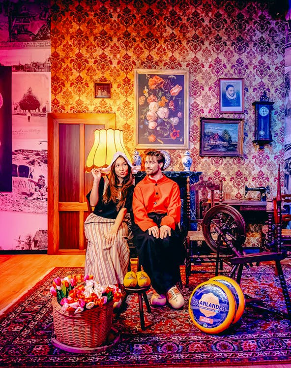 Guests in traditional Dutch attire with tulips and cheese in Holland-themed room.