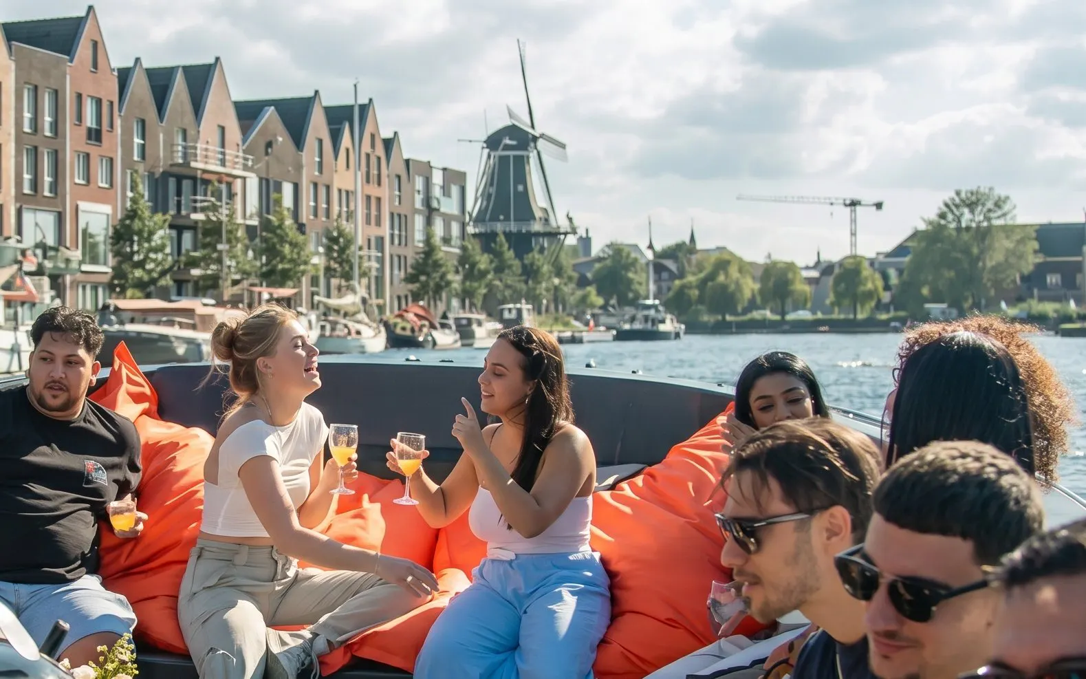 People enjoying drinks on a boat tour in Haarlem with a windmill and canal houses in the background.