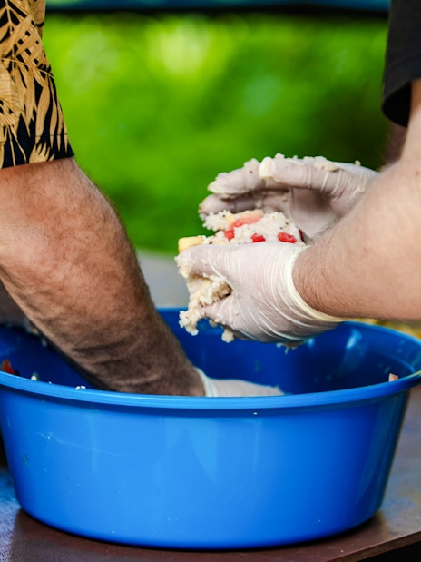 Hands shaping rice balls in a blue bowl at Bukit Elephant Park.