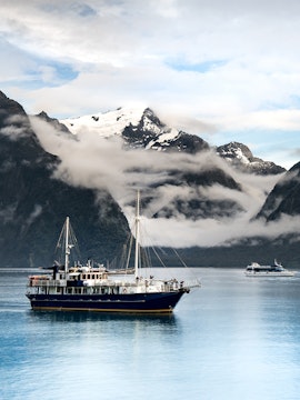 Cruise ship sailing through Milford Sound with snow-capped mountains in the background.