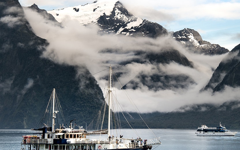 Cruise ship sailing through Milford Sound with snow-capped mountains in the background.