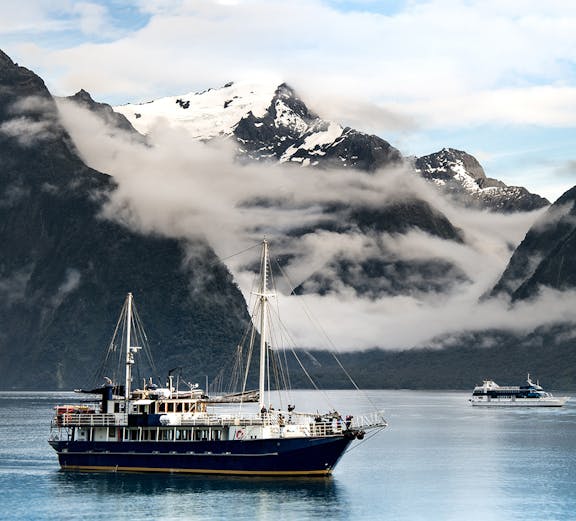 Cruise ship sailing through Milford Sound with snow-capped mountains in the background.