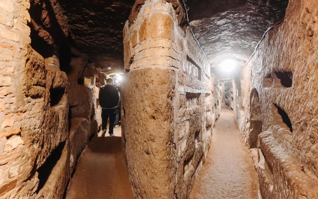 Rome catacombs corridor with visitors exploring ancient passageways.