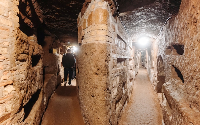 Rome catacombs corridor with visitors exploring ancient passageways.