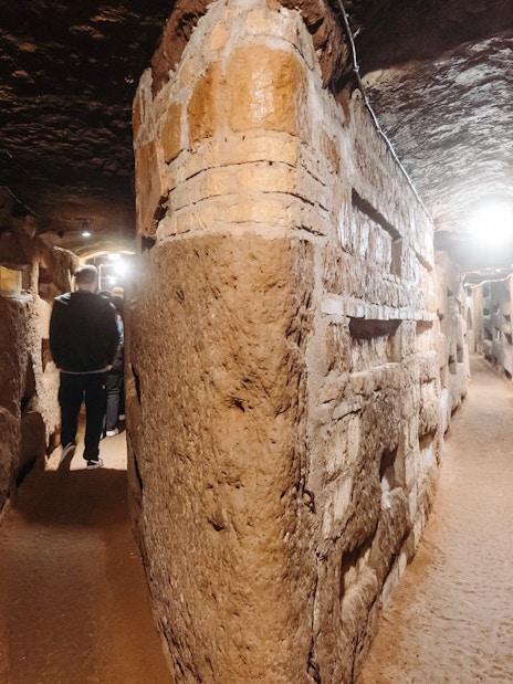 Rome catacombs corridor with visitors exploring ancient passageways.