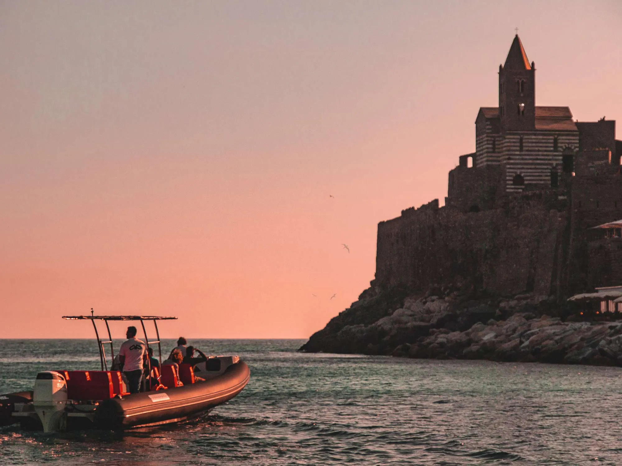 Boat approaching Portovenere church at sunset, La Spezia boat trip.