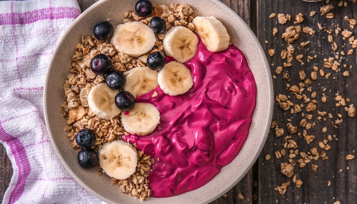 Bowl with tasty acai smoothie and fresh granola on wooden table