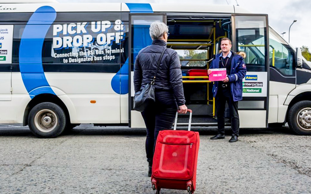 Tourist with luggage assisted by staff at Reykjavik Keflavik airport shuttle.