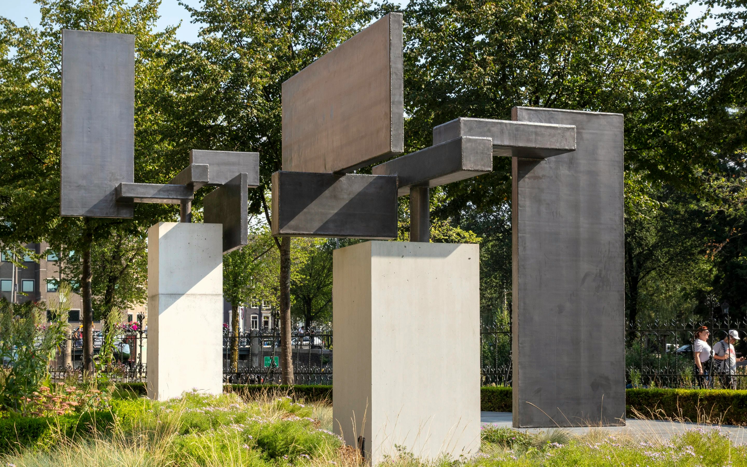 Modern abstract sculpture by Carel Visser in a park setting, featuring geometric metal forms.