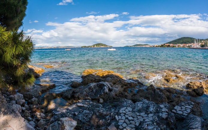 Rocky shoreline with view of Osljak island and boats in Croatia.