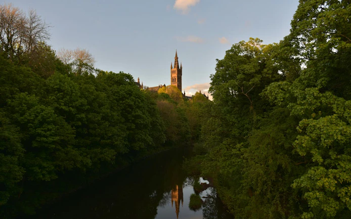 University of Glasgow tower above lush trees and river, Historic Glasgow exploration game.