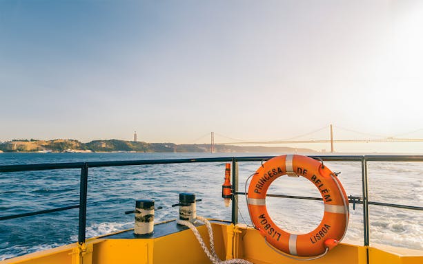 Hop On Hop Off boat with view of Lisbon's 25 de Abril Bridge and Cristo Rei statue.