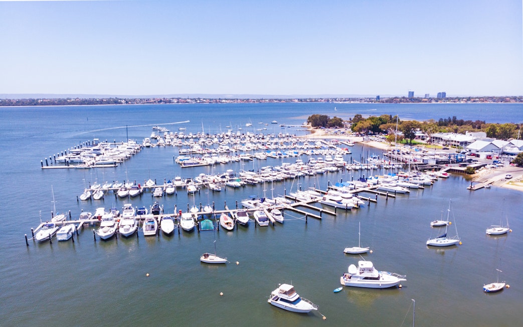 Boats docked at Royal Perth Yacht Club marina with city skyline in the background.