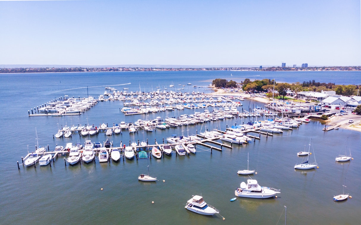 Boats docked at Royal Perth Yacht Club marina with city skyline in the background.