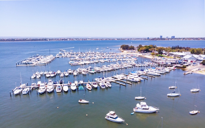 Boats docked at Royal Perth Yacht Club marina with city skyline in the background.